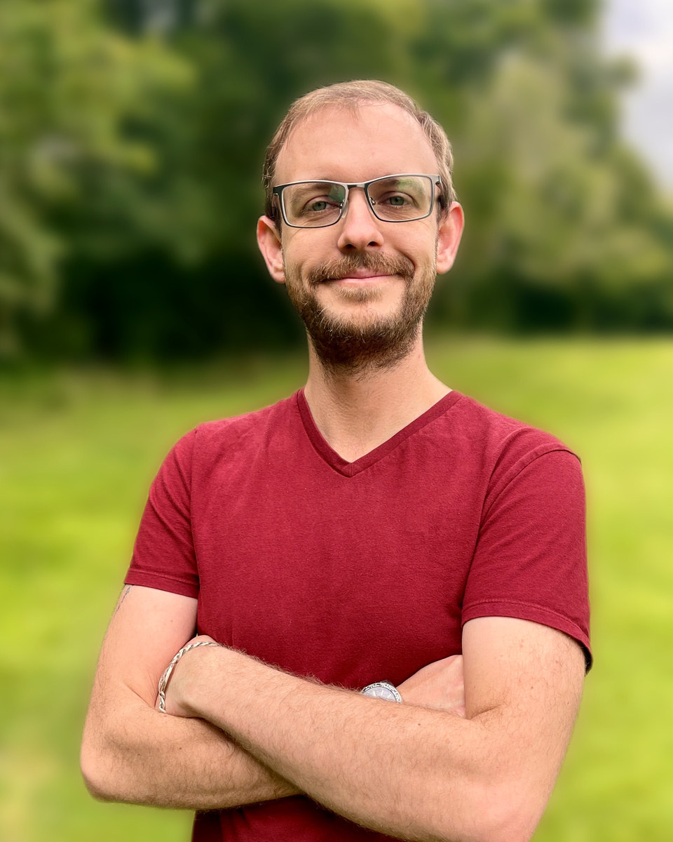 Cassidy, Guardian Vista's independent Medicare broker, arms crossed outdoors at a park in a red v-neck shirt.